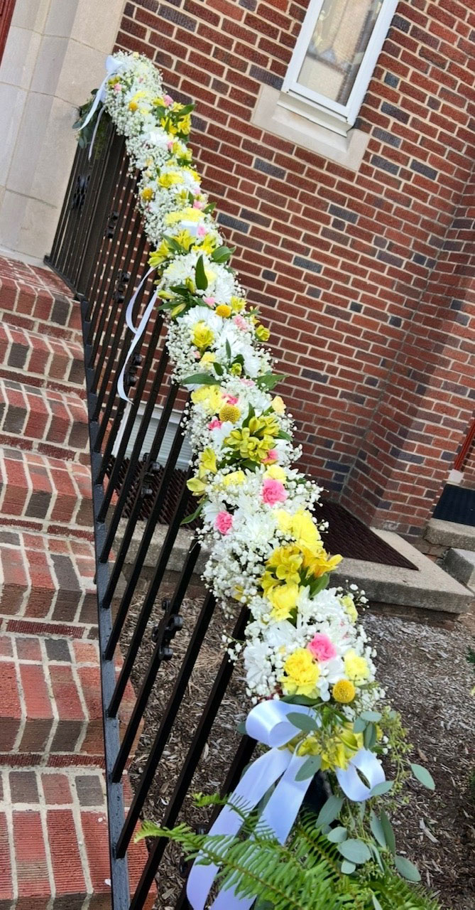Wedding floral garland of daisies, baby's breath, and ribbon draped along a church railing